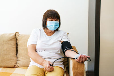 An elderly woman wearing mask measures her blood pressure with an electronic