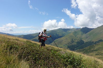 Senior woman walking on hill against sky