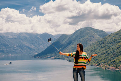 Woman taking selfie while standing at lake against mountains