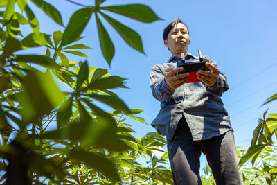 Low angle view of man holding smart phone against sky