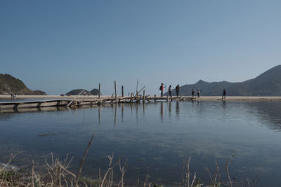 People on lake against clear blue sky