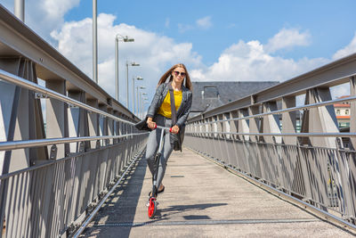 Smiling teenage girl riding push scooter on footbridge 