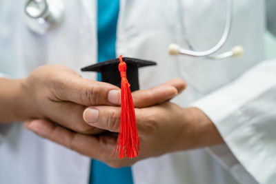 Midsection of female doctor holding mortarboard