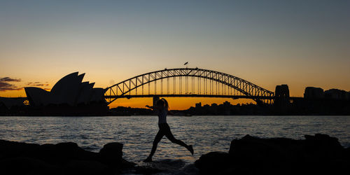 Silhouette bridge over bay against sky during sunset