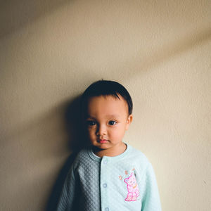 Close-up portrait of baby boy standing by beige wall