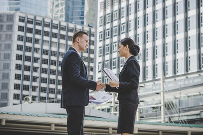 Business people giving handshake while standing against building