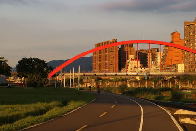 Road by bridge and buildings against sky during sunset