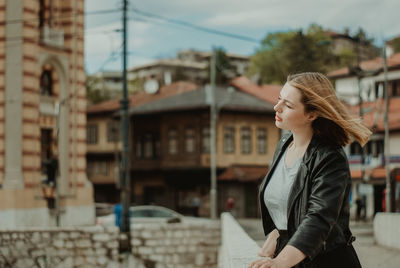 Side view of young woman standing against buildings in city