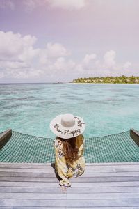 Rear view of woman with hat on beach against sky