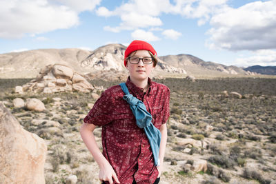 Portrait of teenage boy standing on rock against sky