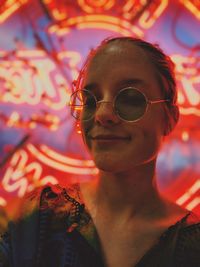 Close-up portrait of woman in sunglasses against illuminated lights