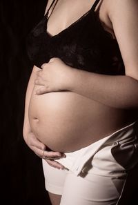 Midsection of woman touching hair over black background