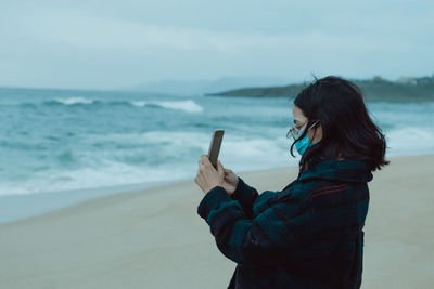 Side view of woman photographing sea against sky