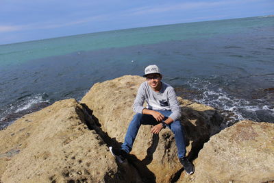 Portrait of man on rock at beach against sky