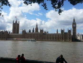 Tourists on riverbank against cloudy sky