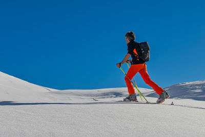 Full length of man skateboarding on snowcapped mountain against clear blue sky