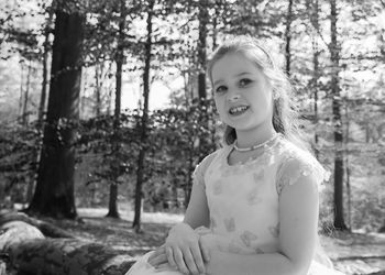 Smiling girl in princess dress sitting against trees at woodland