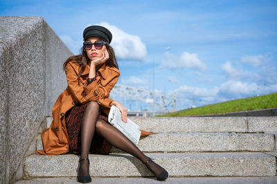 Young woman sits on the steps on the embankment with newspaper in hand