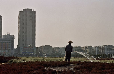 Rear view of man working on farm in city against clear sky