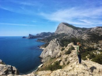 Man standing on rock by sea against sky