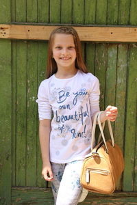 Portrait of smiling girl standing against wooden wall