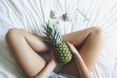 Low section of woman holding pineapple while sitting on bed