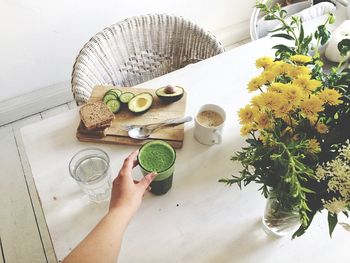 Cropped hand of woman reaching for drink by flowers on table