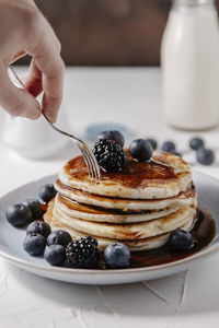 Woman sticking a fork into a stack of homemade pancakes with berries