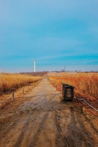 Road leading towards field against blue sky