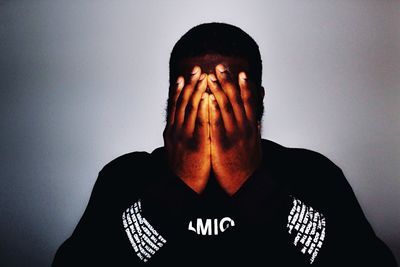 Portrait of man covering face against wall