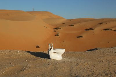 Toilet bowl on sand in desert against sky