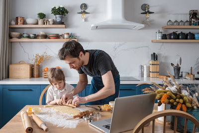 Cute preschool boy and his father baking cookies using video lesson on laptop