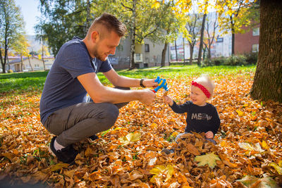 Full length of father playing with daughter while sitting on leaves outdoors