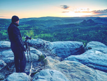 Rear view of man standing on rock against sky during sunset