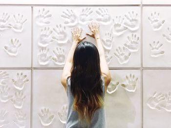 Rear view of woman touching white wall with handprints