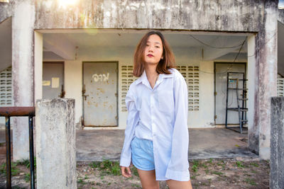 Portrait of young woman standing against building