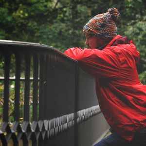 Side view of man wearing red jacket standing by railing