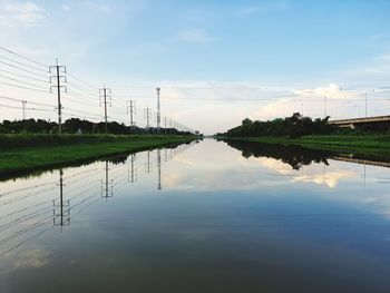 Reflection of electricity pylon in lake against sky