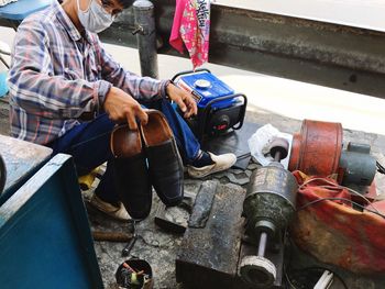 Cobbler holding shoes while sitting on street