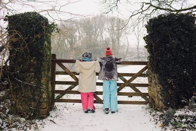 Rear view of siblings standing on snow by gate