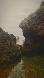 Woman standing on cliff by sea against sky