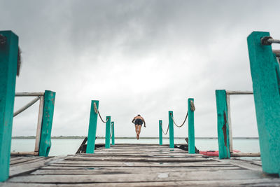 Rear view of woman standing on pier against sky