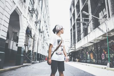 Teenage boy looking away while standing on road amidst buildings in city