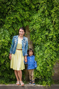 Woman and little handsome baby boy staying surrounded by lush green plants