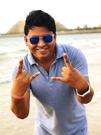 Portrait of smiling man showing horn sign while standing at beach