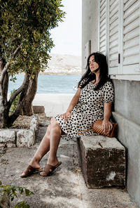 Pretty girl sitting on stone bench under tree. summer, lifestyle, polka dot dress.
