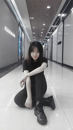 Portrait of woman sitting on tiled floor in corridor