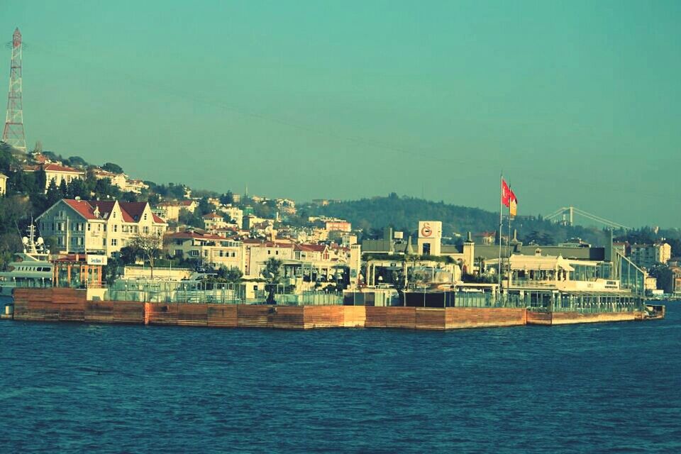 architecture, built structure, building exterior, water, waterfront, clear sky, sea, flag, copy space, city, nautical vessel, river, blue, transportation, boat, day, cityscape, rippled, outdoors, no people