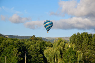 Hot air balloon flying over trees against sky in murol village.