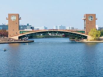 Bridge over river by buildings against clear sky